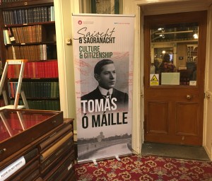 A poster stands in a room displaying the Saíocht & Saoránacht exhibition for Irish language professor Tomás Ó Máille.