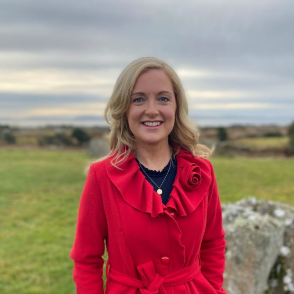 Dr Niamh O'Brien wearing a red coat and standing outdoors with a green field in the background.