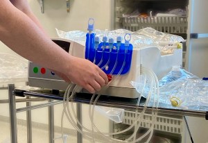 Peritoneal dialysis machine on a silver table in a hospital setting. A dialysis nurse is setting up the machine by attaching the tubing.
