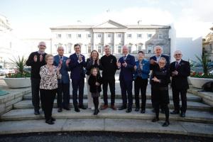 A group of people standing outside the front of the Irish parliament building clapping as they celebrate the passing of the Human Tissue Bill. The group includes 11 adults (3 of whom are women) and 1 child. It includes the Minister for Health Stephen Donnolly