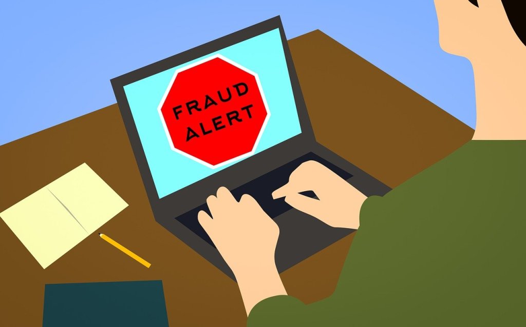 Cartoon style image of a computer with a red hexagon on the screen with the words “Fraud Alert”
