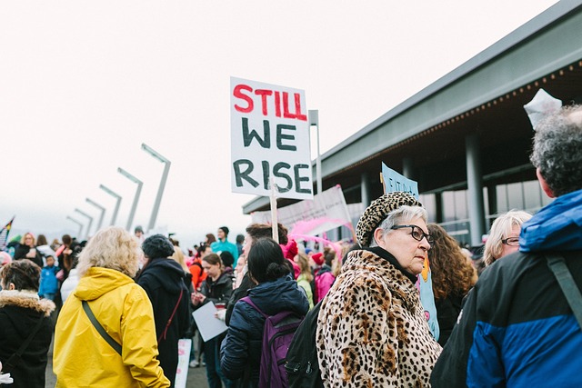 A crowd of protestors standing with one visible sign that says "Still we rise!"