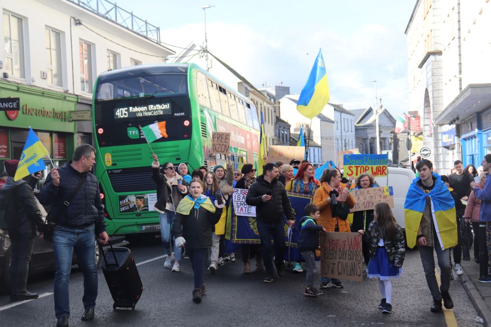 Crowd of people draped in Ukrainian flags walking down the road