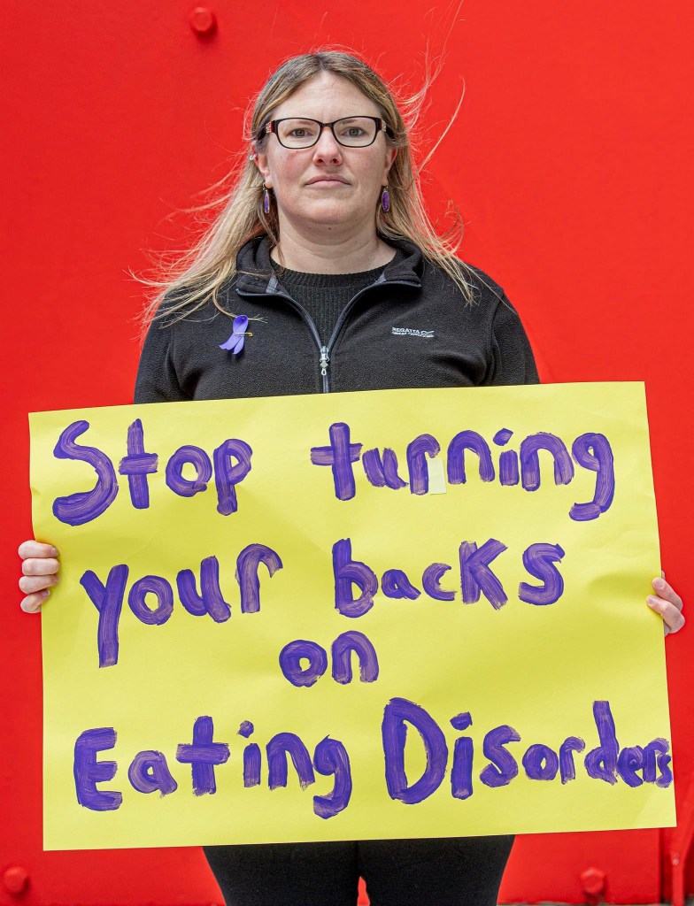 Woman holding a sign that reads “Stop turning your backs on Eating Disorders”