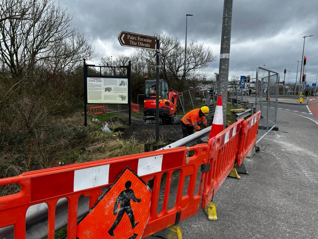 Roadworks on the side of a road, surrounding by red barriers to remove a gate